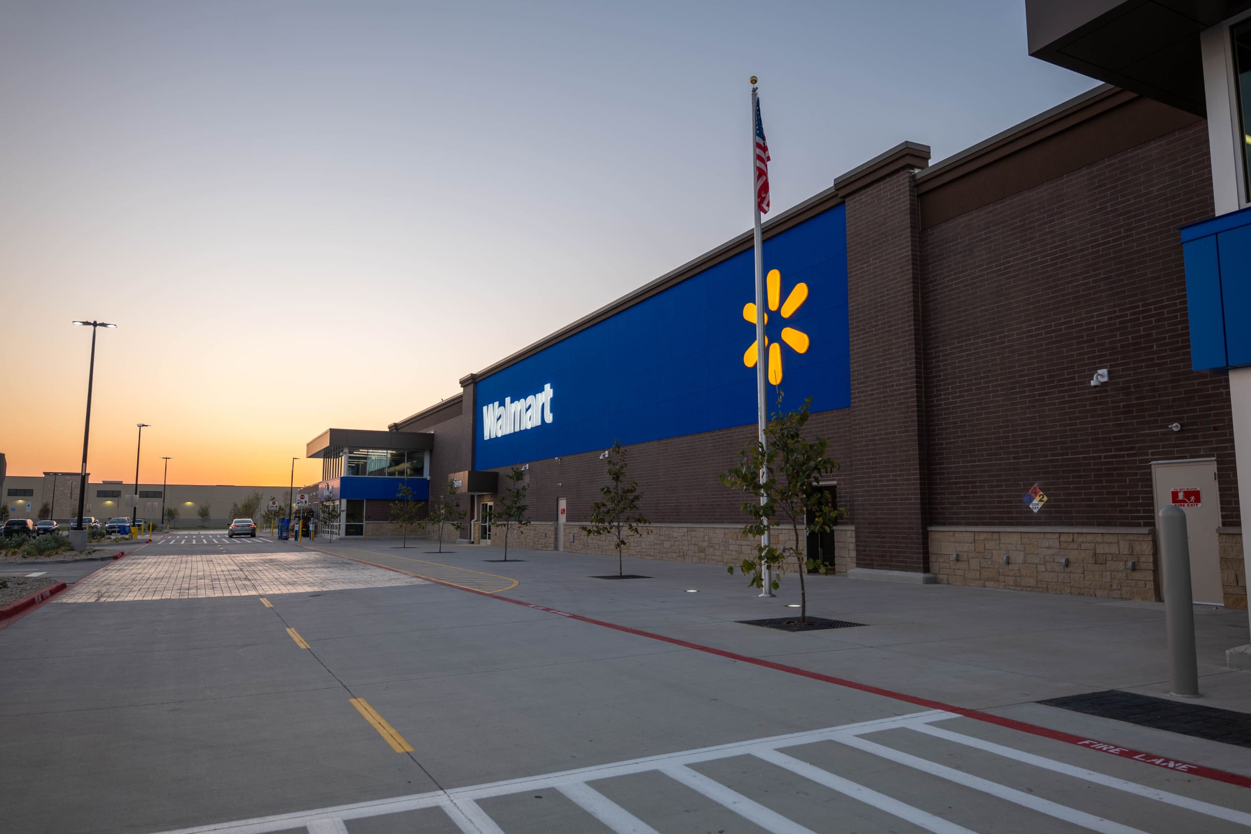 The exterior of a Walmart store at sunset, with blue signage, an American flag, and an empty parking area—similar to scenes near Home Depot San Antonio West Construction sites.