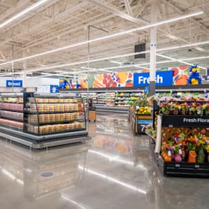 A brightly lit grocery store produce section displays fresh fruits, vegetables, pre-packaged salads, and a stand of assorted floral bouquets, reminiscent of the vibrant atmosphere at Home Depot San Antonio West Construction.