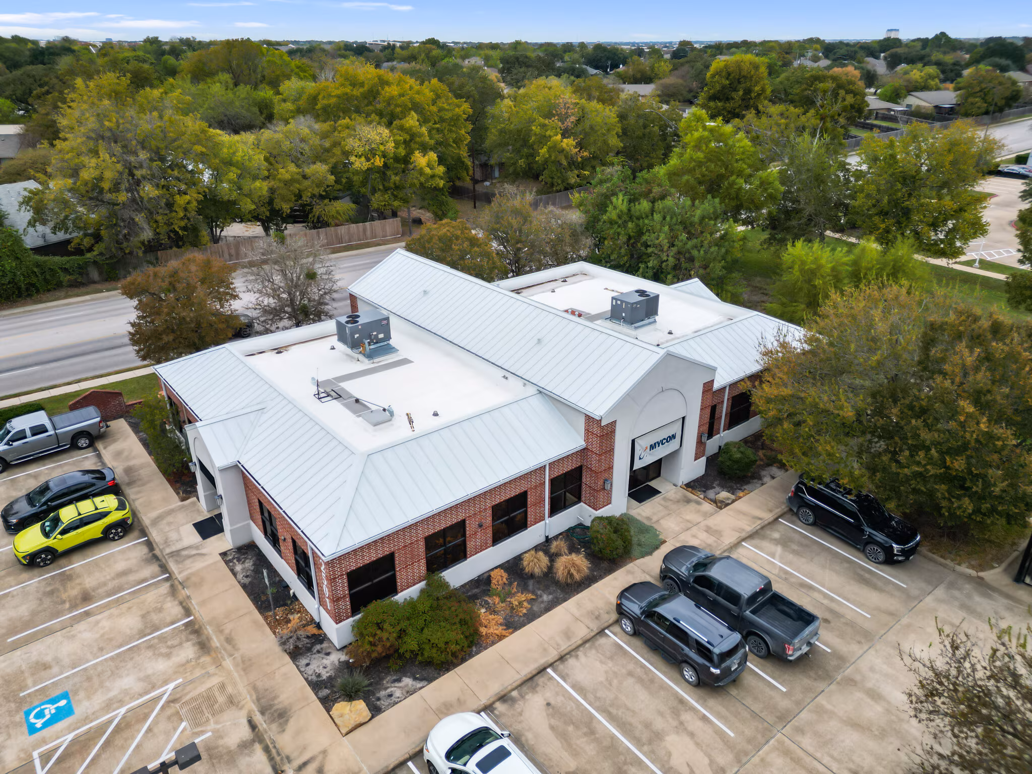 Aerial view of a one-story brick office building with a metal roof, surrounded by trees and parked cars in a parking lot—perfect for businesses seeking reputable general contractors near me.