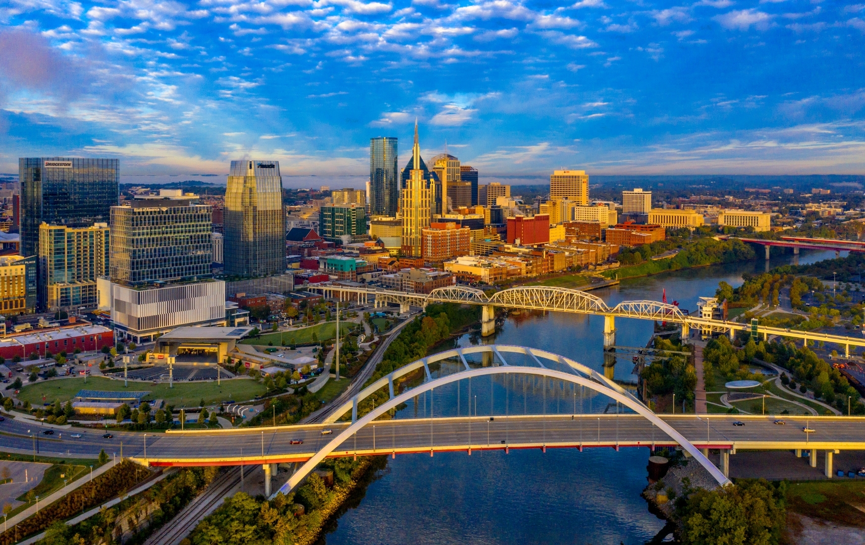 Aerial view of downtown Nashville, Tennessee, showing modern buildings—many constructed by general contractors near me—bridges over the Cumberland River, and a partly cloudy sky.